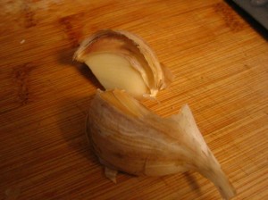 garlic clove on wooden cutting board, partly peeled