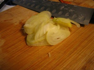 Shallot sliced thinly, resting on cutting board with knife